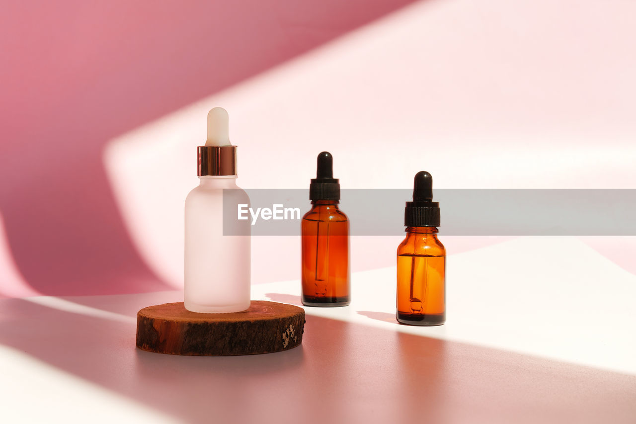 Banner of three transparent amber and frozen glass dropper bottles on pink background