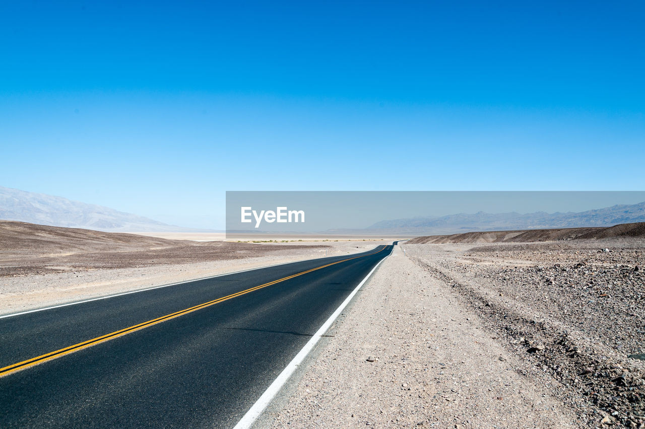 Empty road against clear blue sky