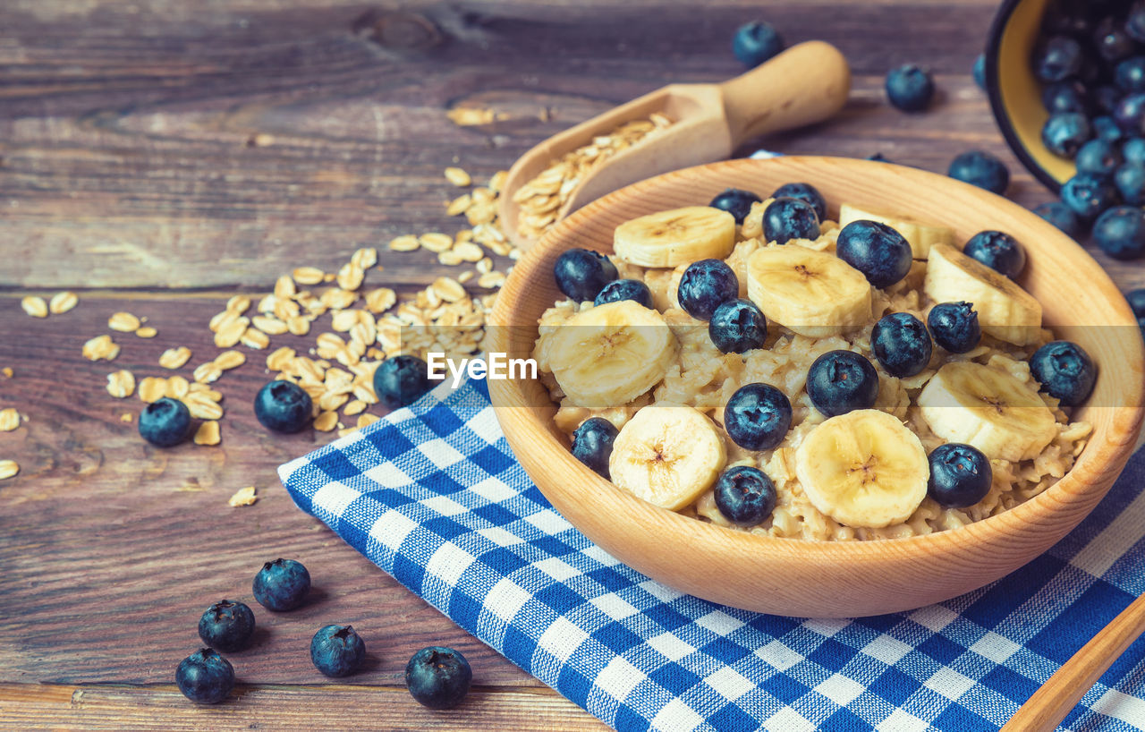 Oatmeal with blueberries and banana in wooden bowl on rustic wooden background. healthy breakfast.