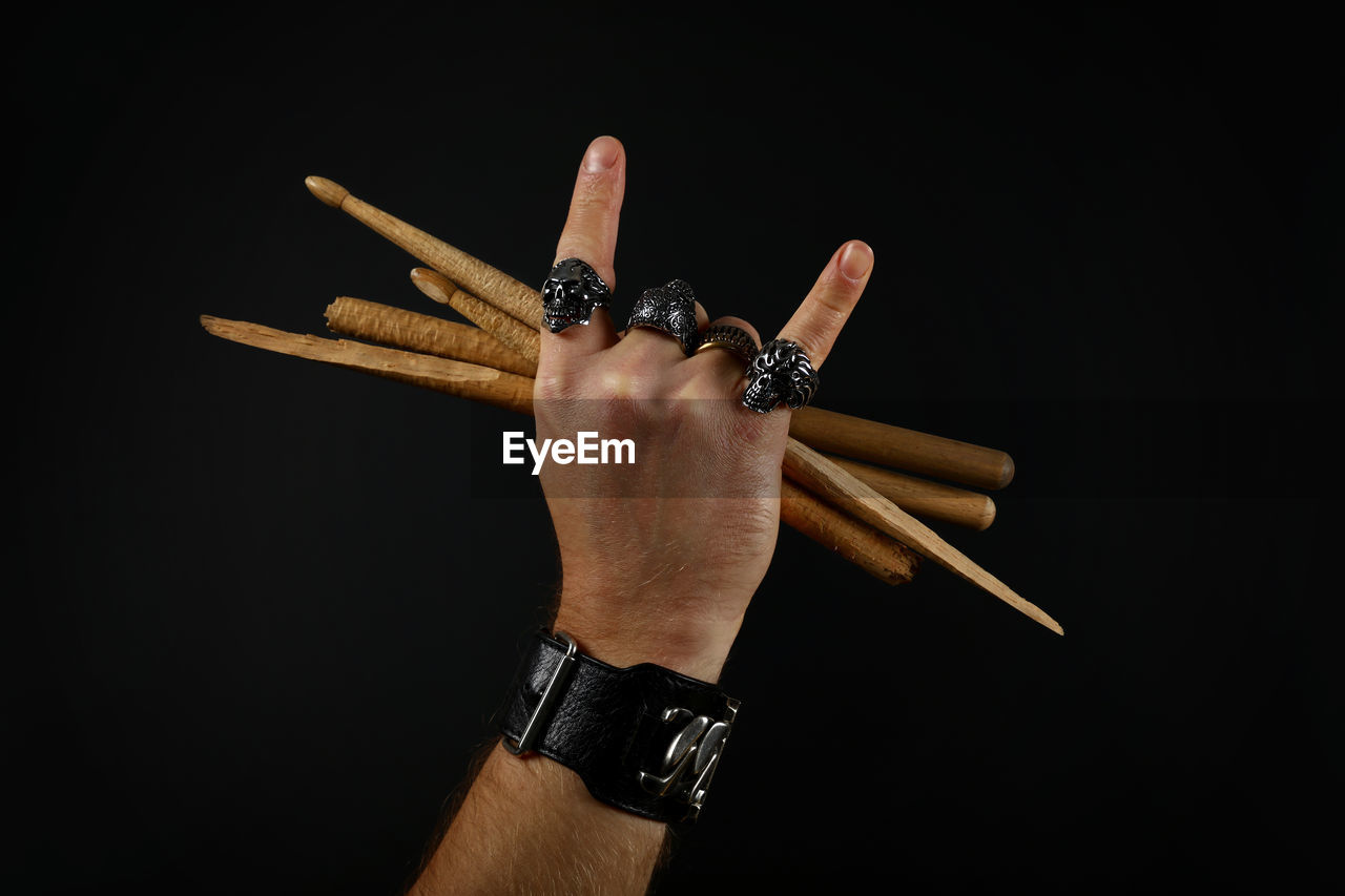 Cropped hand of man holding sticks over black background