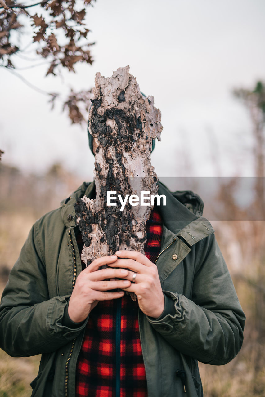 Man covering face with wood while standing in forest