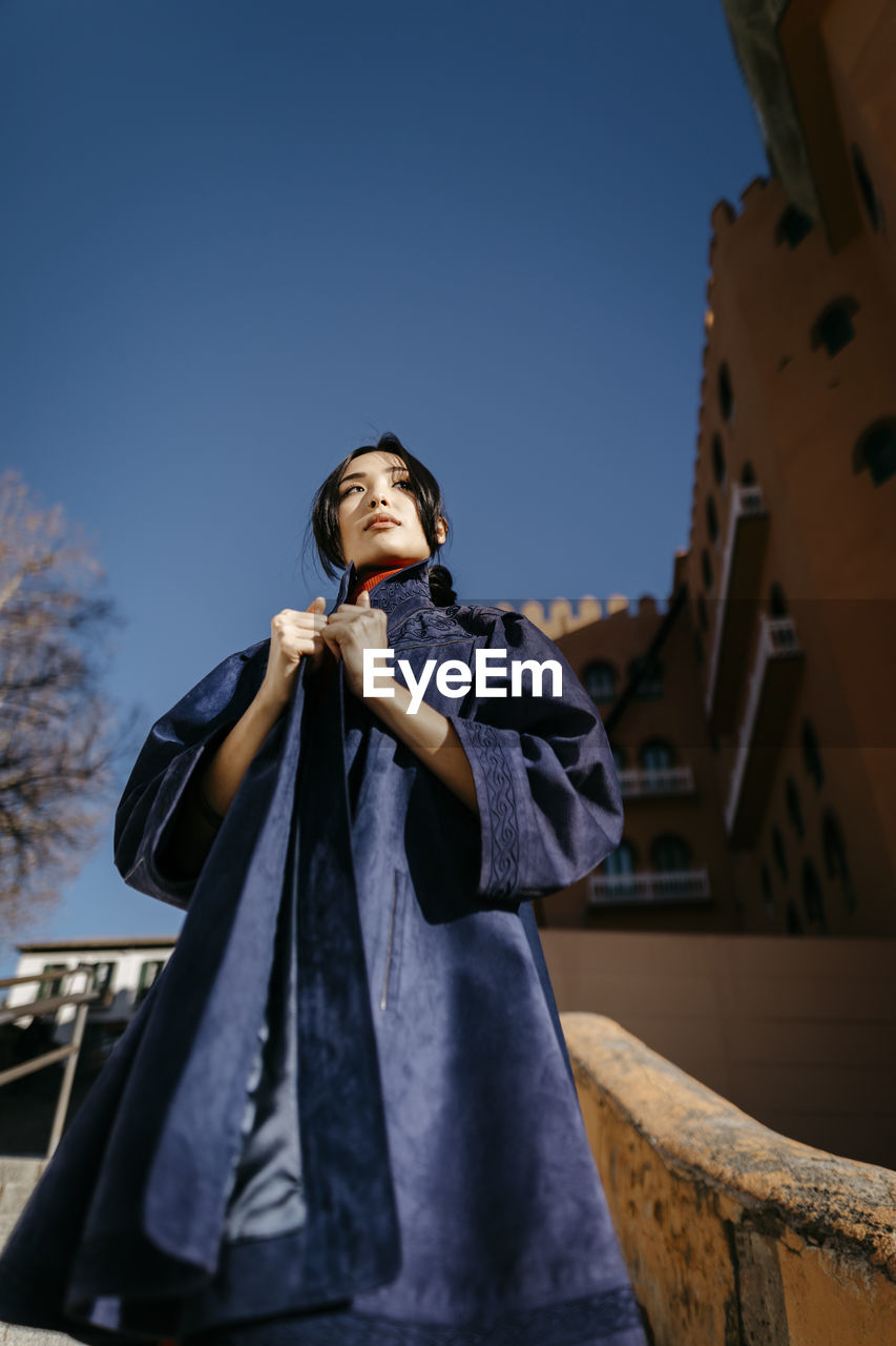 Young woman wearing coat looking away during sunny day