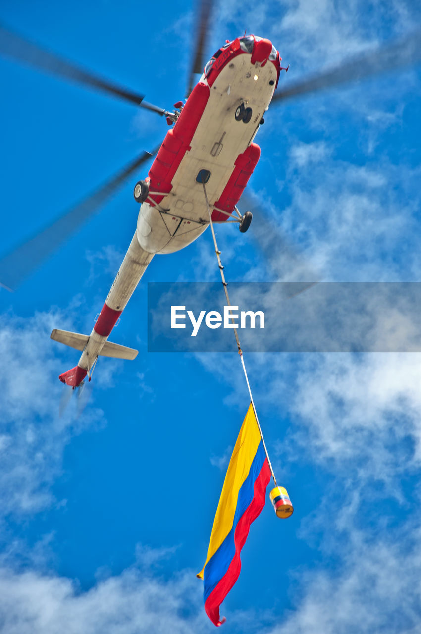 Low angle view helicopter hovering against cloudy sky