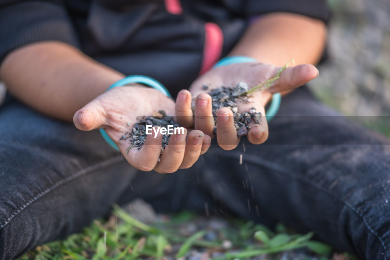 Midsection of man holding pebble sitting on grass