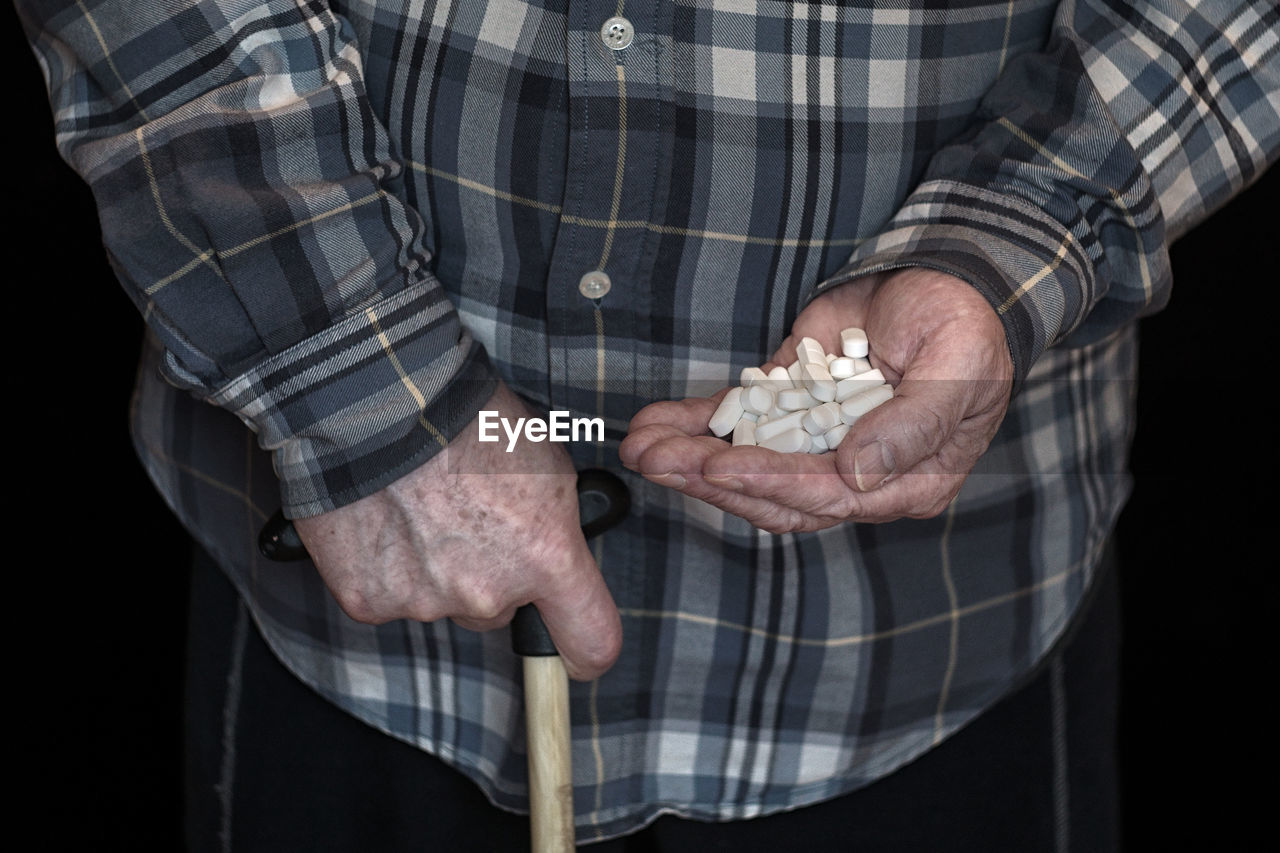 Midsection of man holding medicine over black background