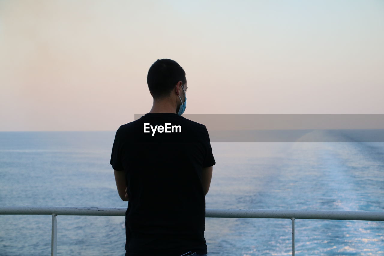 Rear view of man on a boat looking at sea against sky