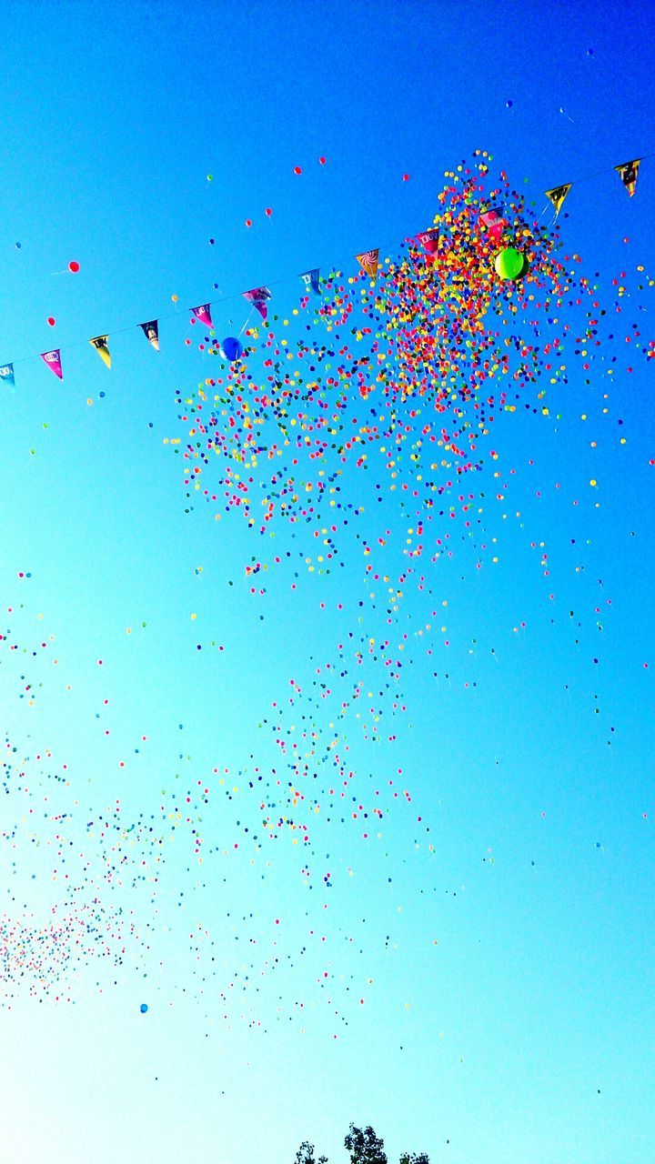 Low angle view of colorful helium balloons flying against blue sky