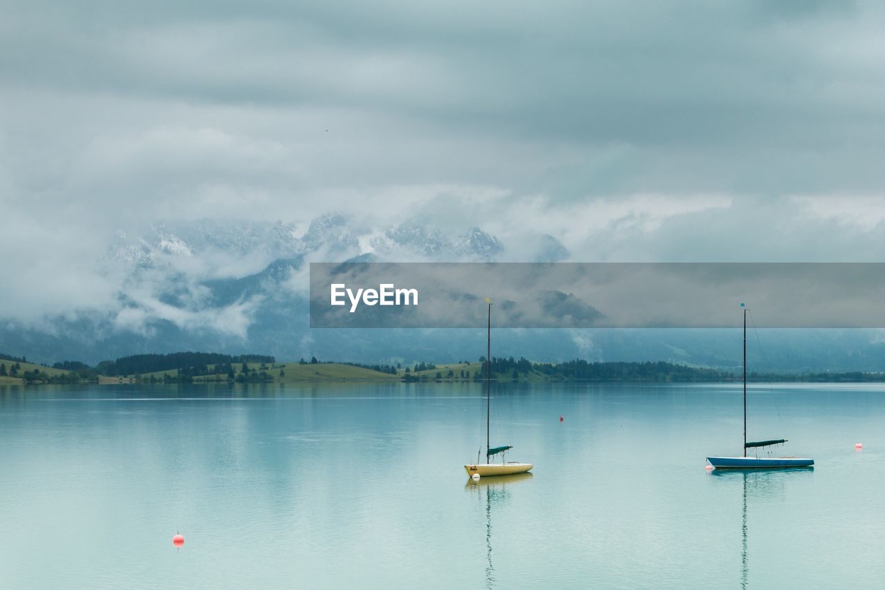 Boats in lake against cloudy sky