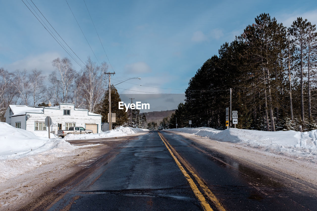 Road by trees against sky during winter