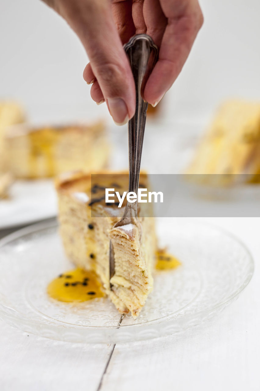 Cropped hand cutting dessert with fork on table