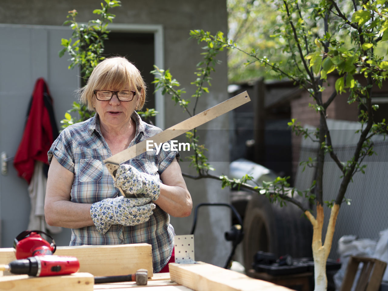 Senior caucasian woman assembles a wooden frame of building using metal fasteners using screwdriver