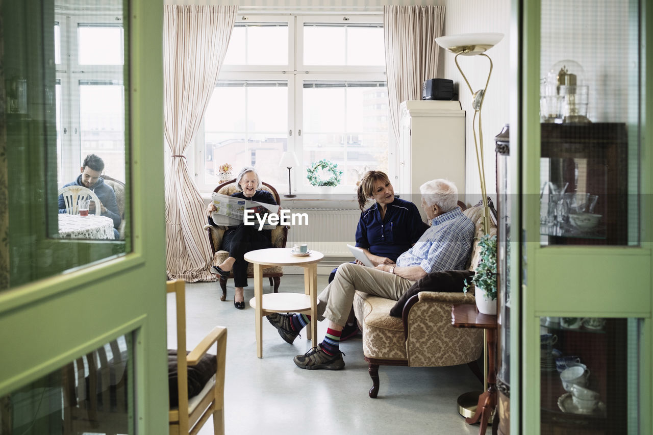 Caretakers with senior couple sitting in living room at nursing home