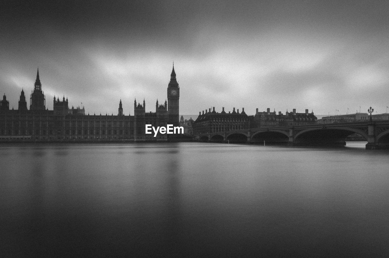 View of the houses of parliament  by river against cloudy sky.