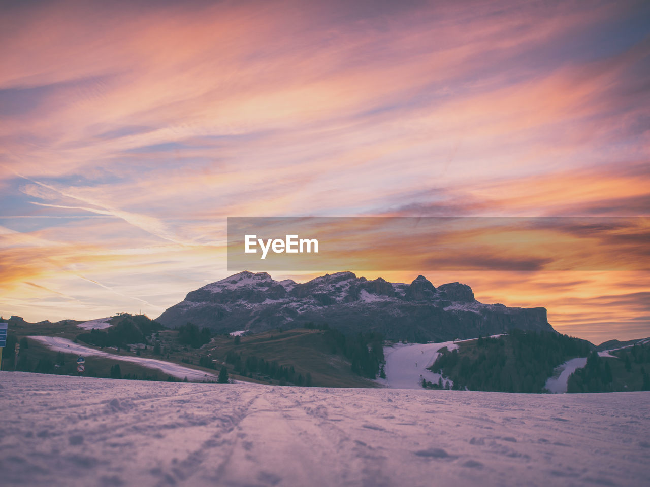 Scenic view of snow covered field by rocky mountains against sky during sunset