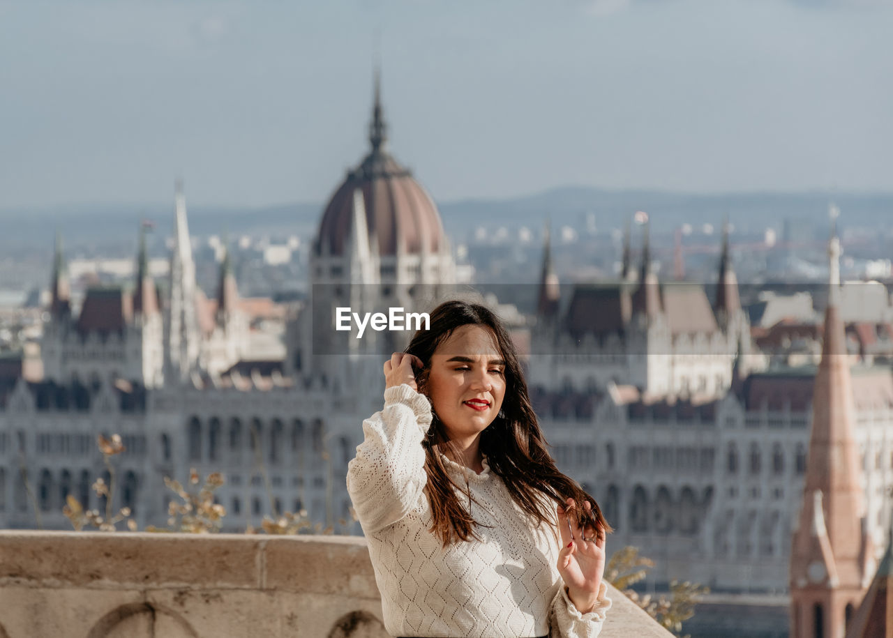 Portrait of beautiful young woman on balcony overlooking hungarian parliament in budapest, hungary