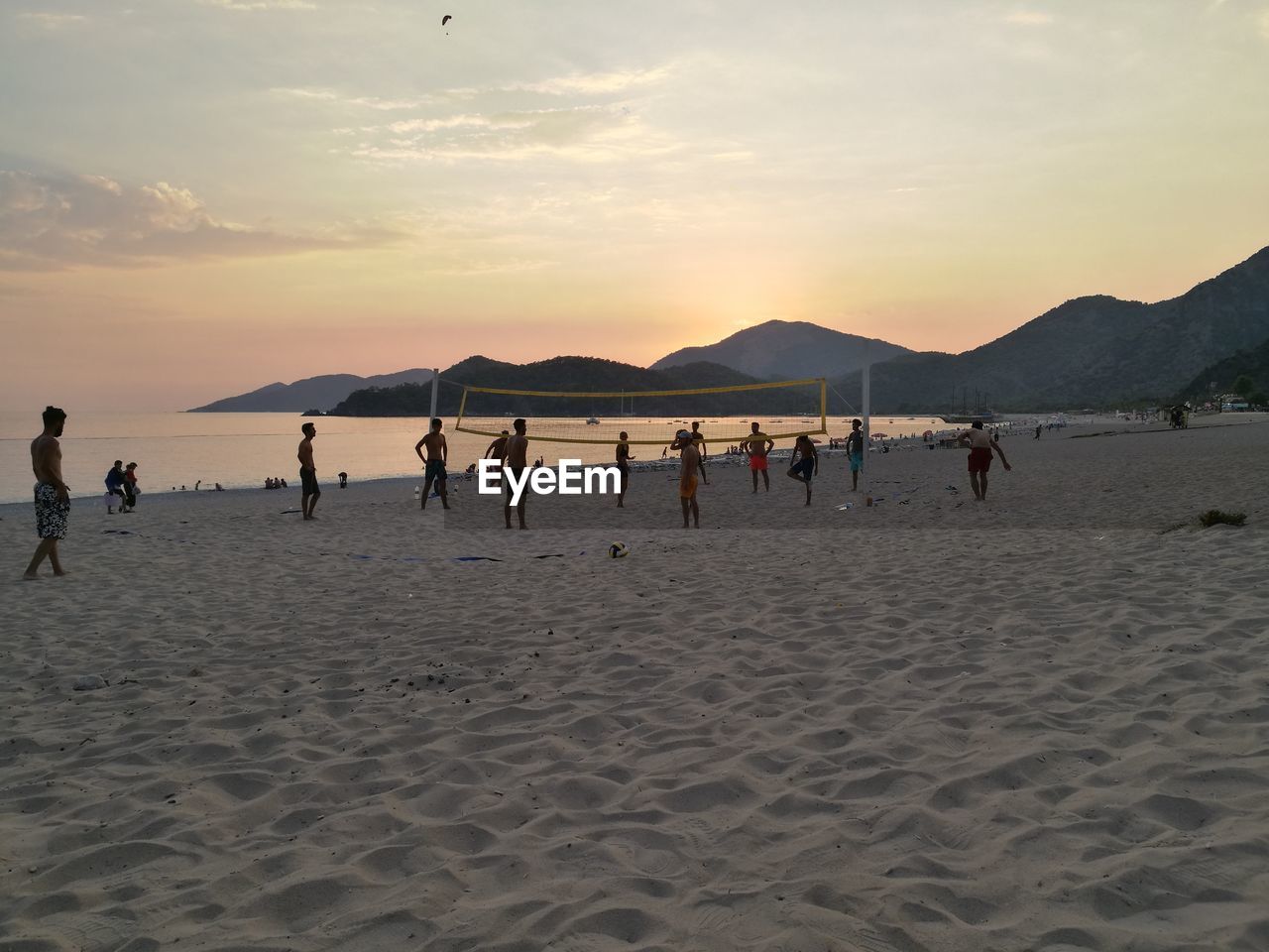 People playing at beach against sky during sunset