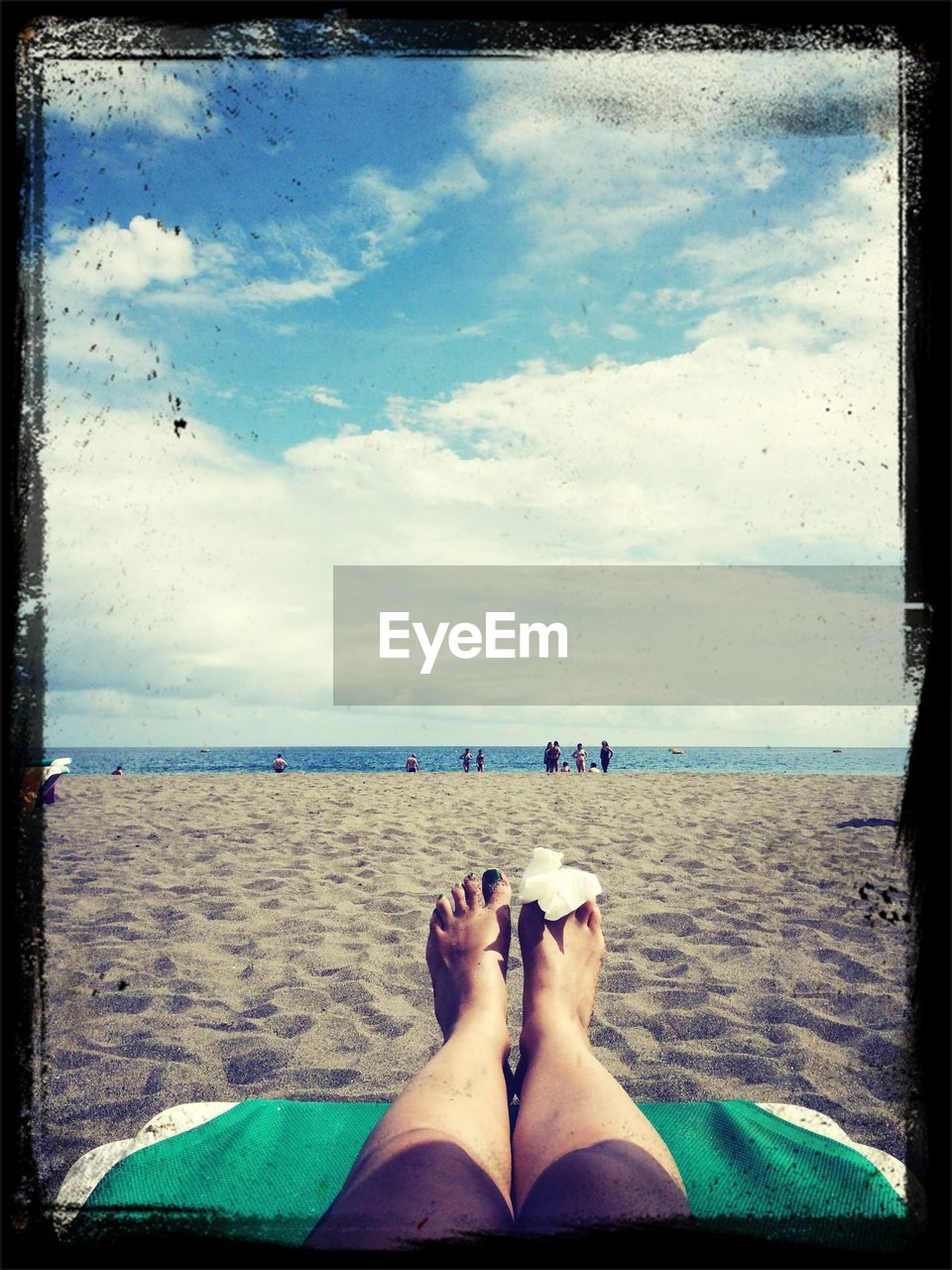 Low section of woman with wounded leg on beach against cloudy sky