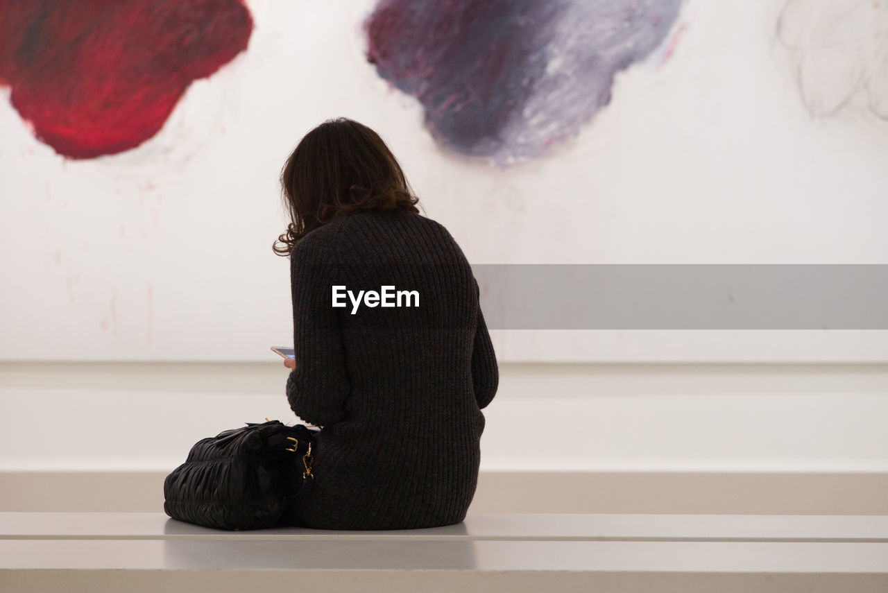 REAR VIEW OF WOMAN STANDING AGAINST CURTAIN