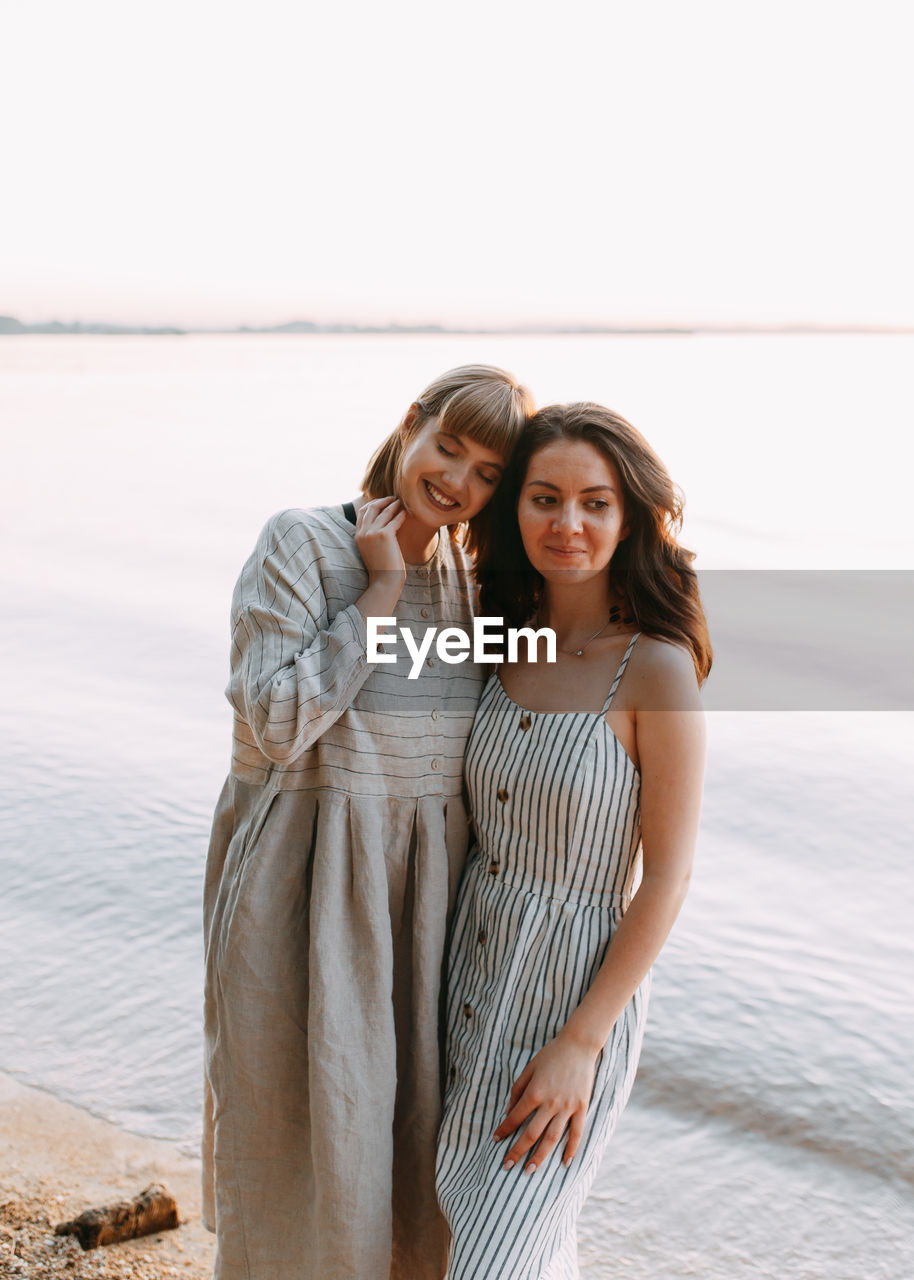 Two relaxing happy smiling girls in summer sundresses by the sea