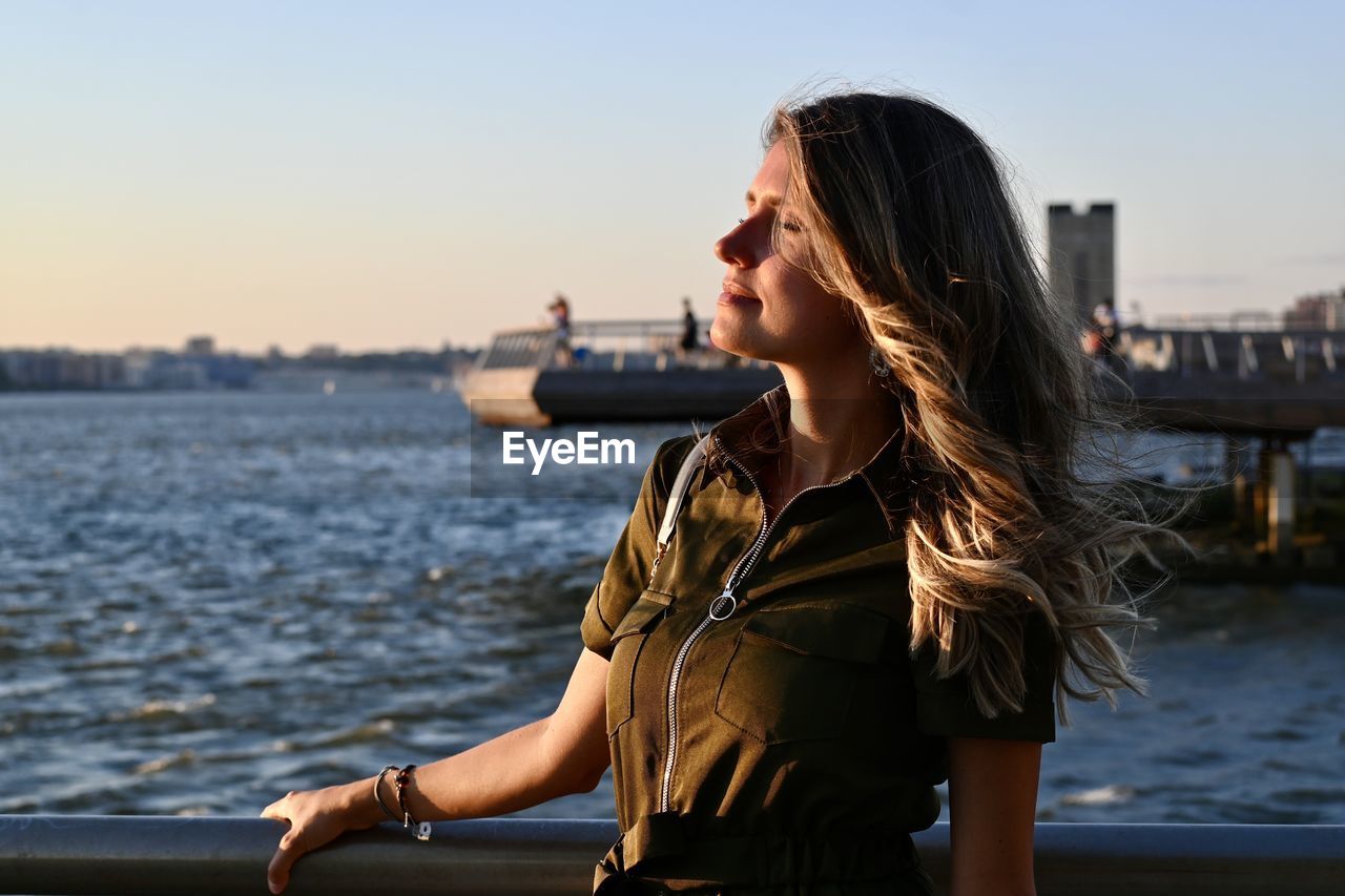 Young woman standing by sea during sunset