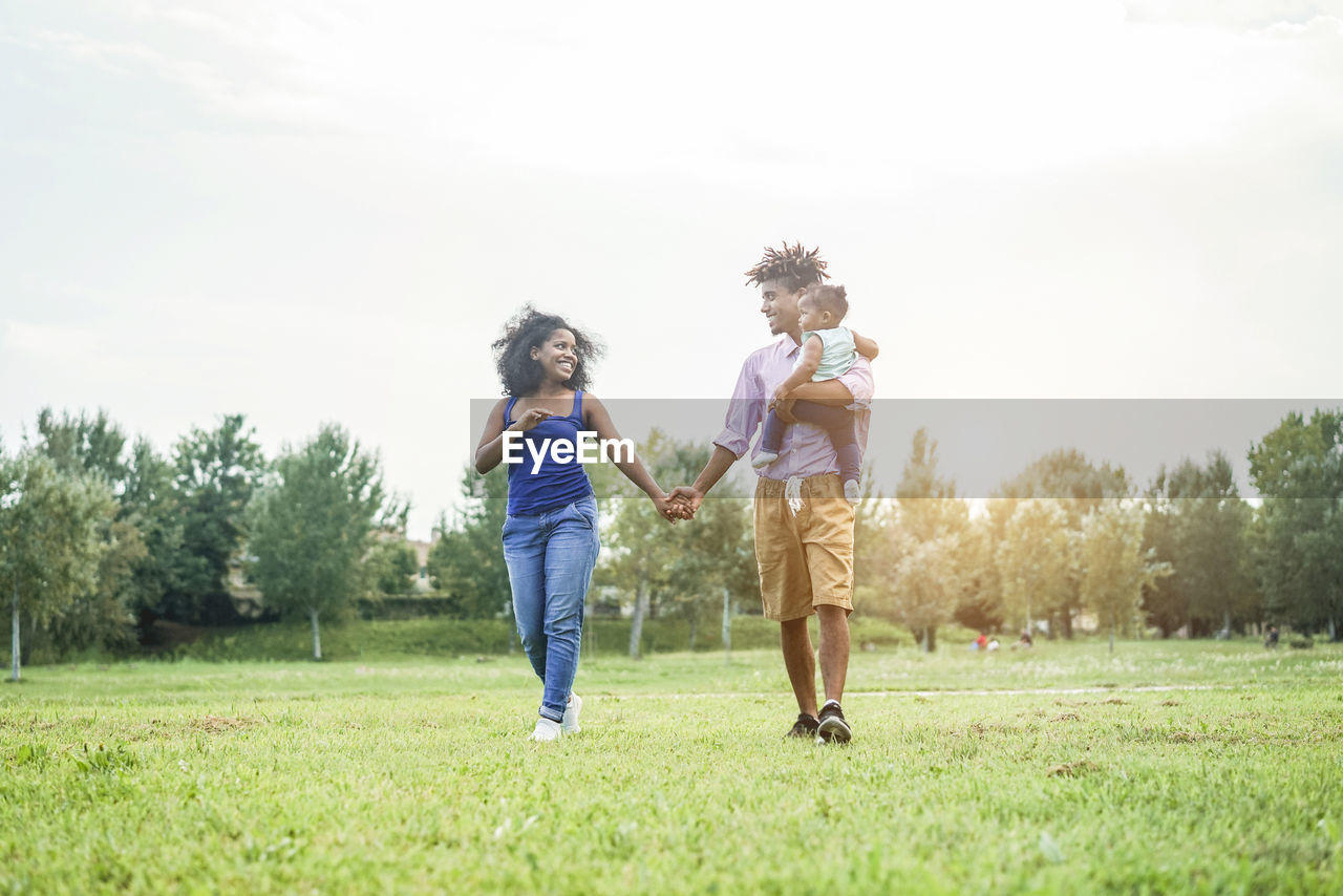 Full length of parents with baby girl walking together on field against sky