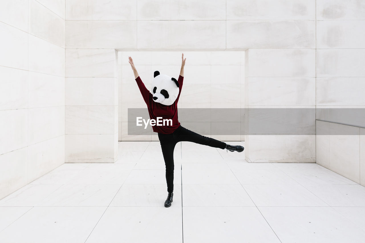 Woman wearing panda mask with arms raised standing against doorway