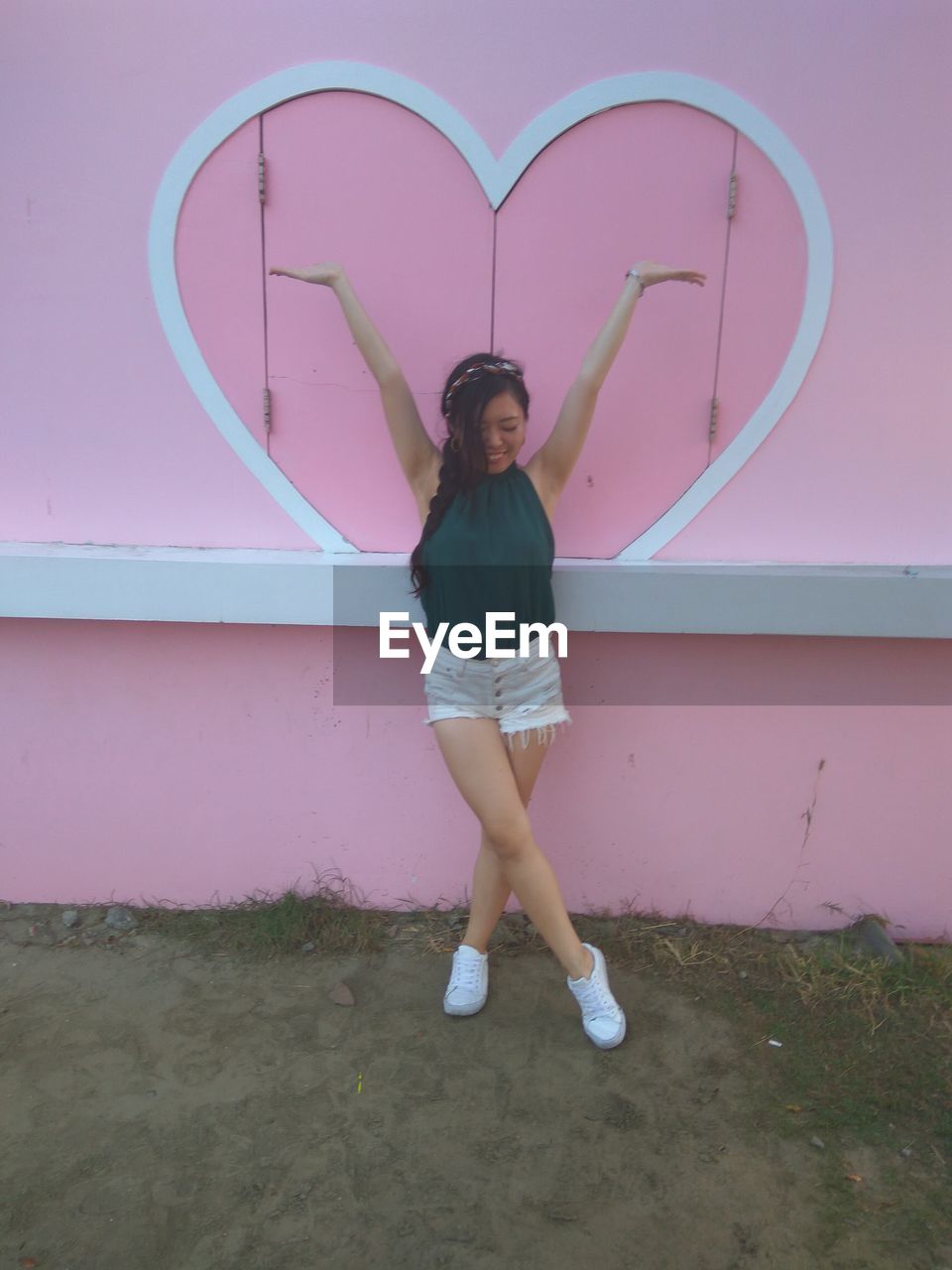 Woman with arms raised standing against heart shape on pink wall