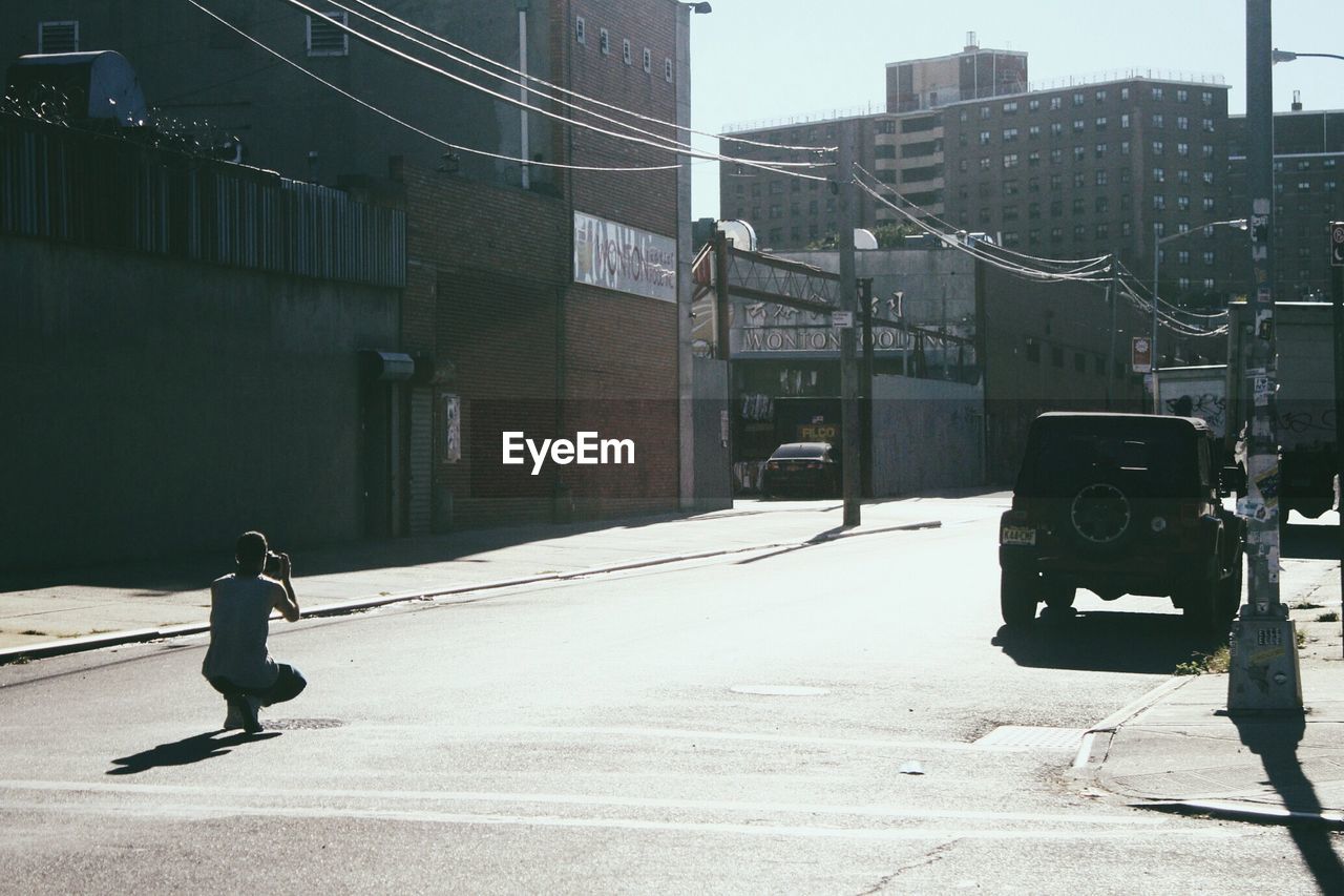 Rear view of man photographing while crouching on city street