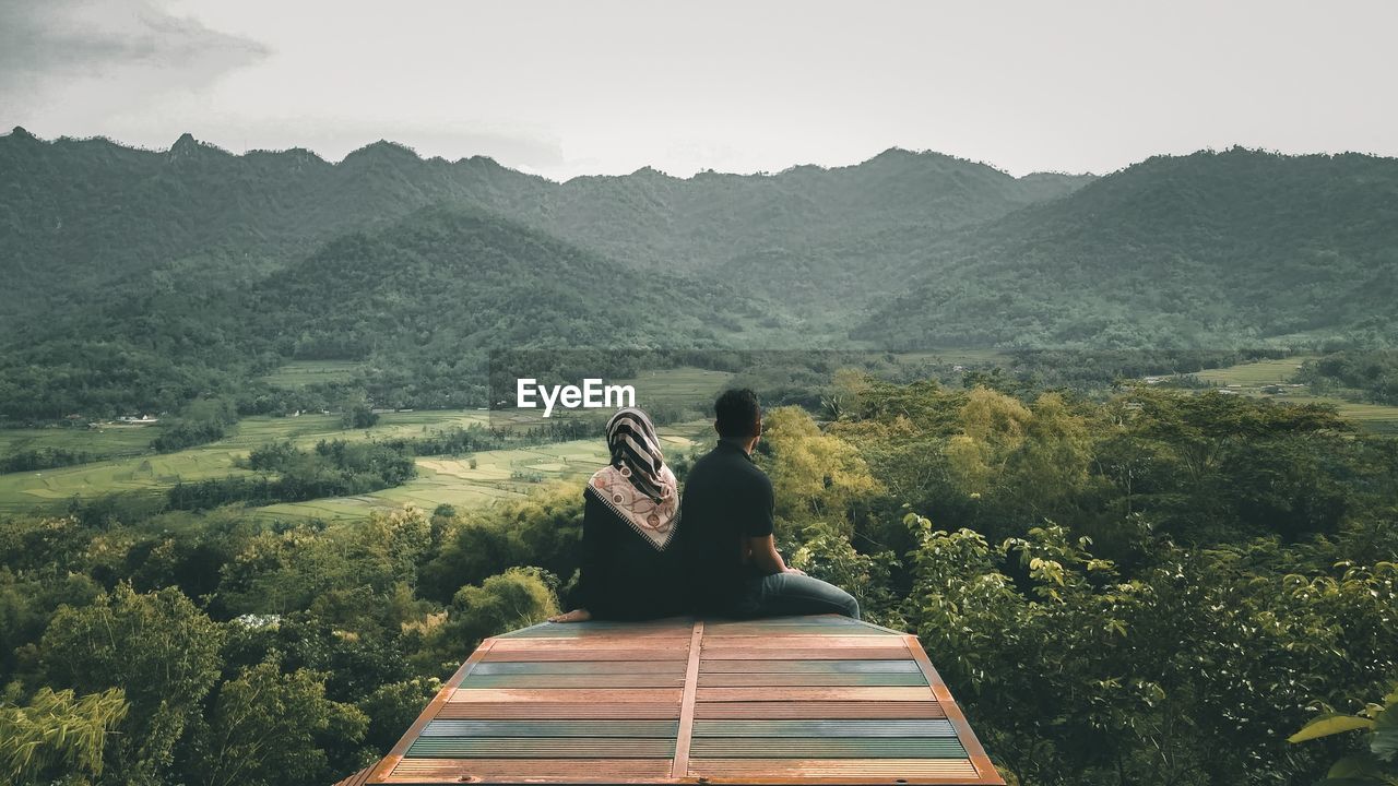 Couple sitting at observation point against sky