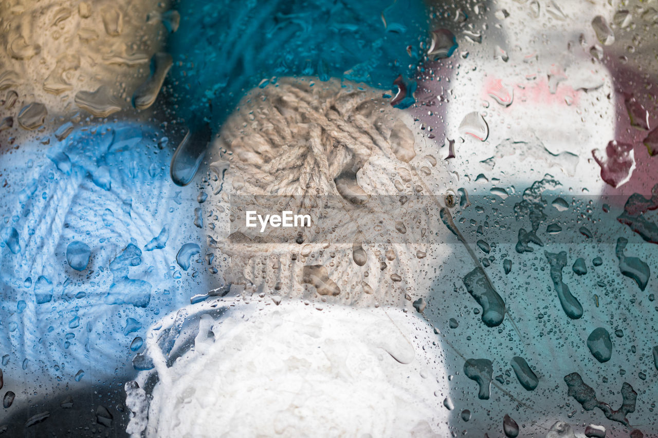 Close-up of colorful yarn balls seen through wet glass window