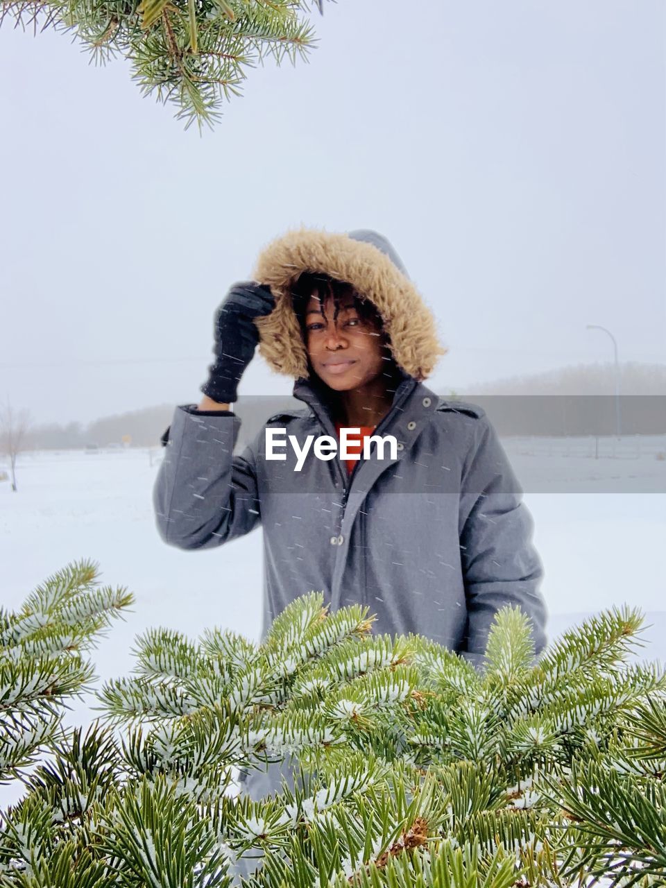 Portrait of woman standing by tree during winter
