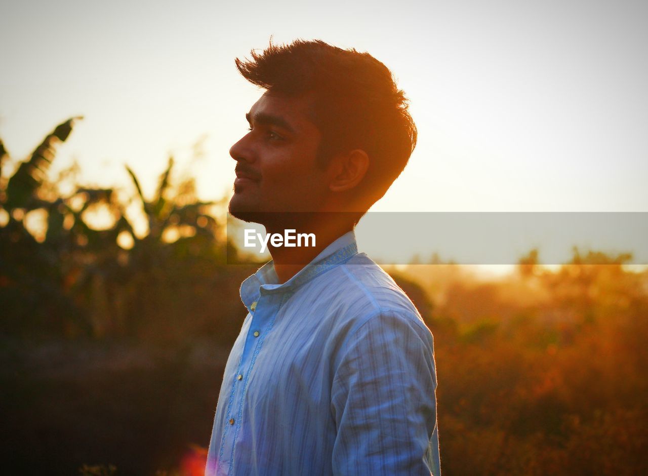 Young man standing against sky during sunset