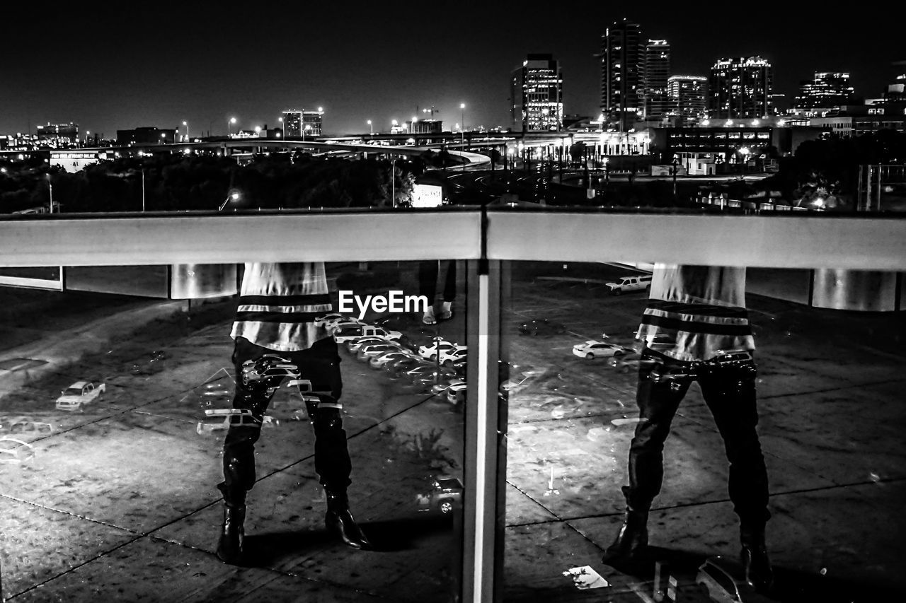 Reflection of person on glass fence at night in city