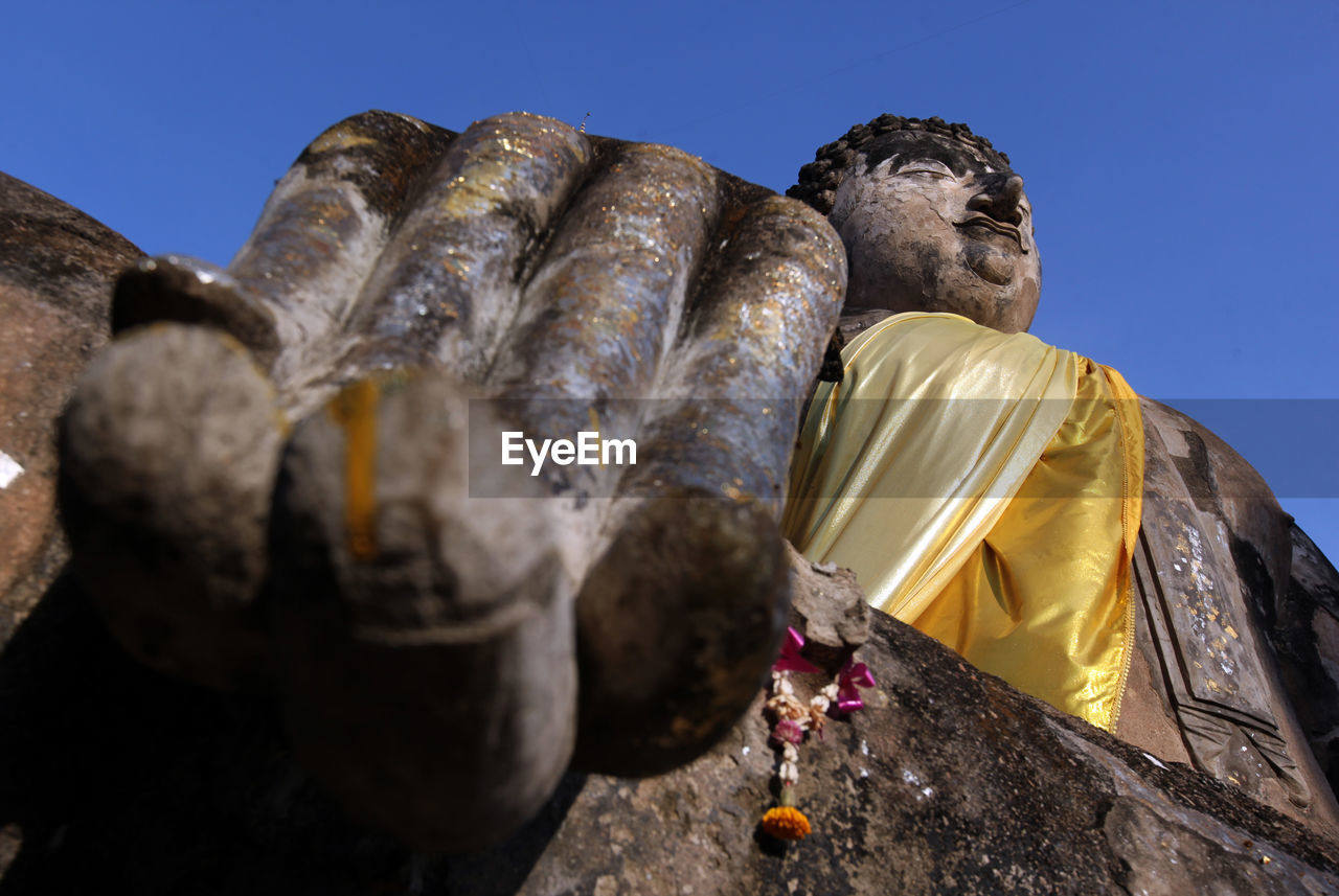 Low angle view of weathered buddha statue against clear sky