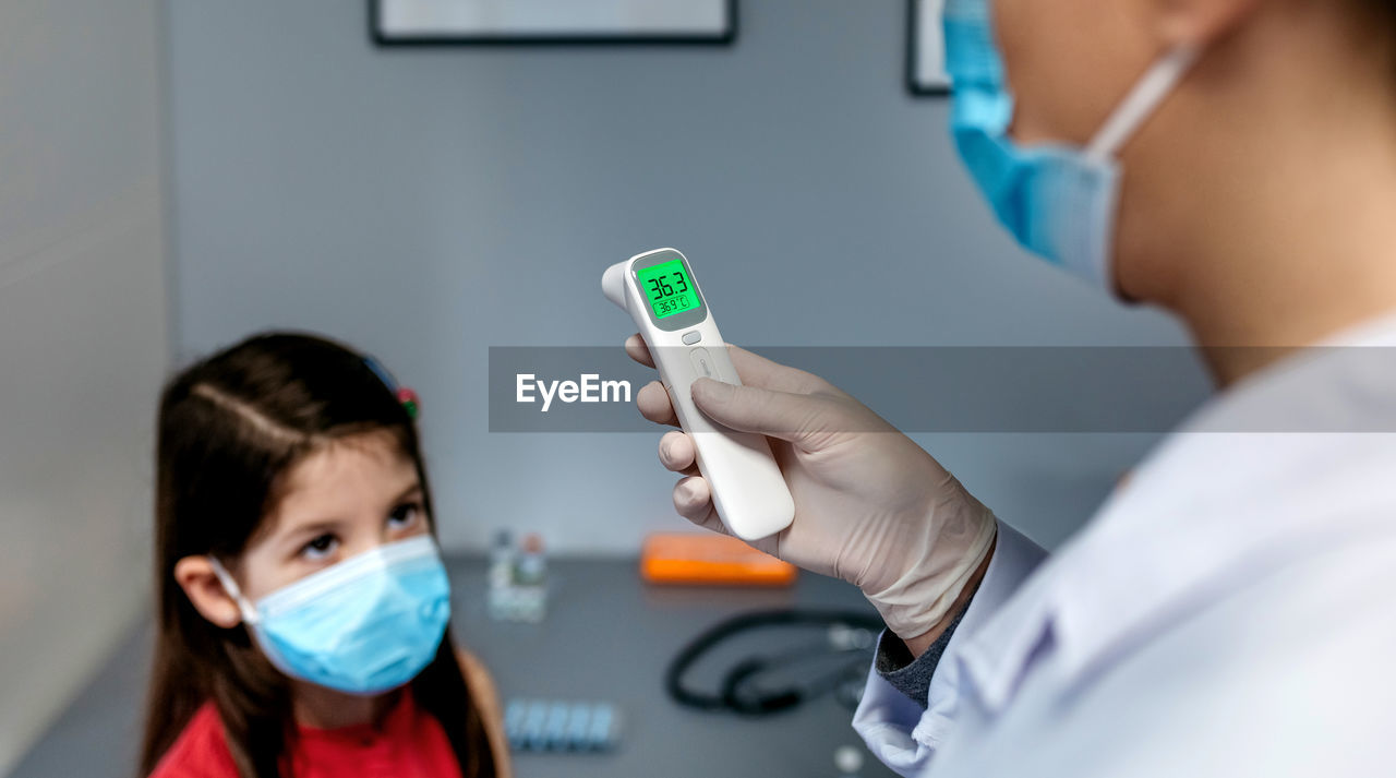 Female doctor looking at infrared thermometer after taking tempe