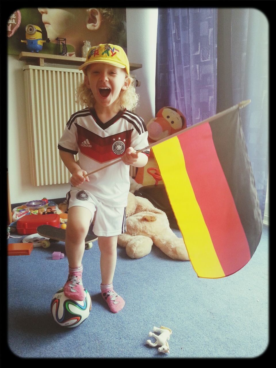 Portrait of playful boy with soccer ball holding german flag at home