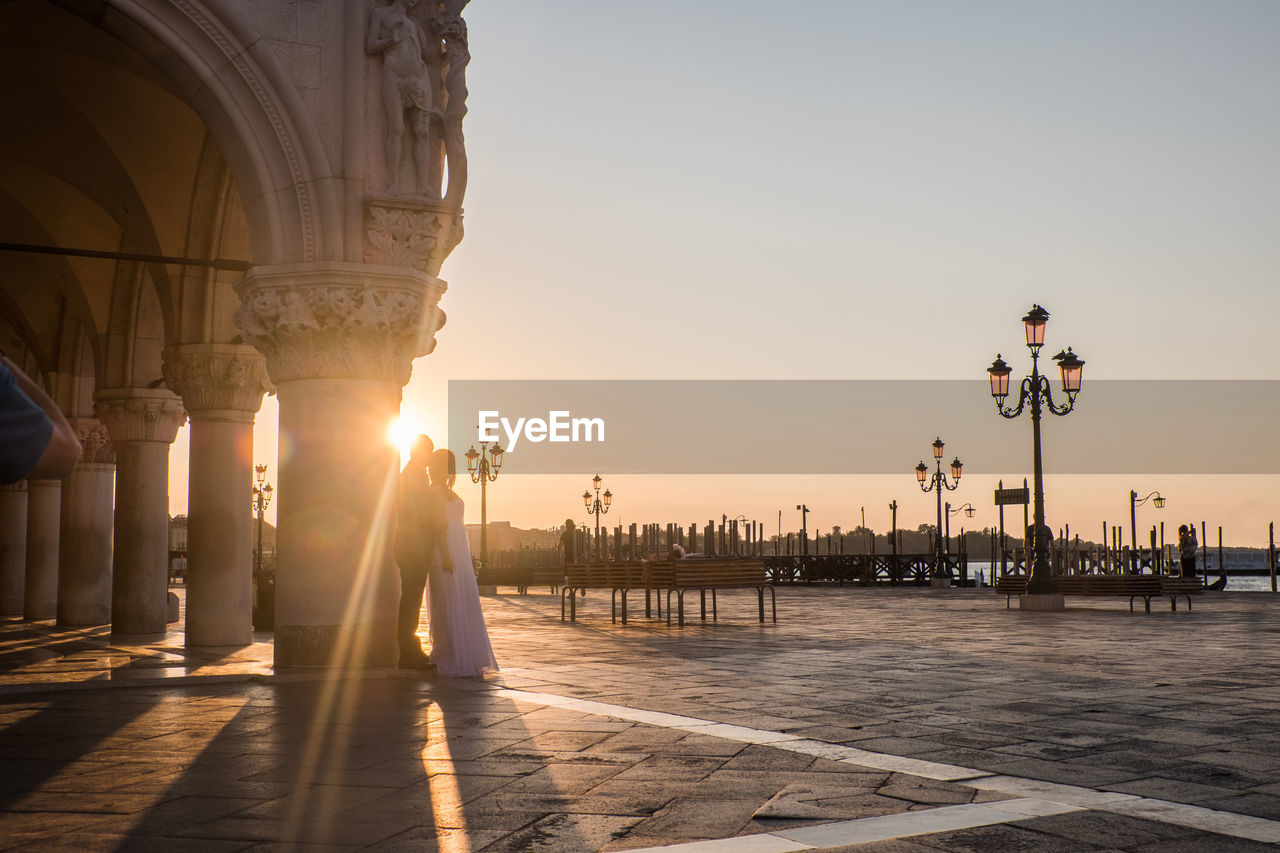 Couple standing by column on street during sunset