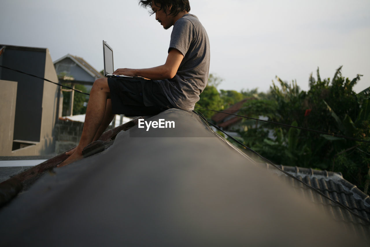 Side view of man sitting and working on rooftop