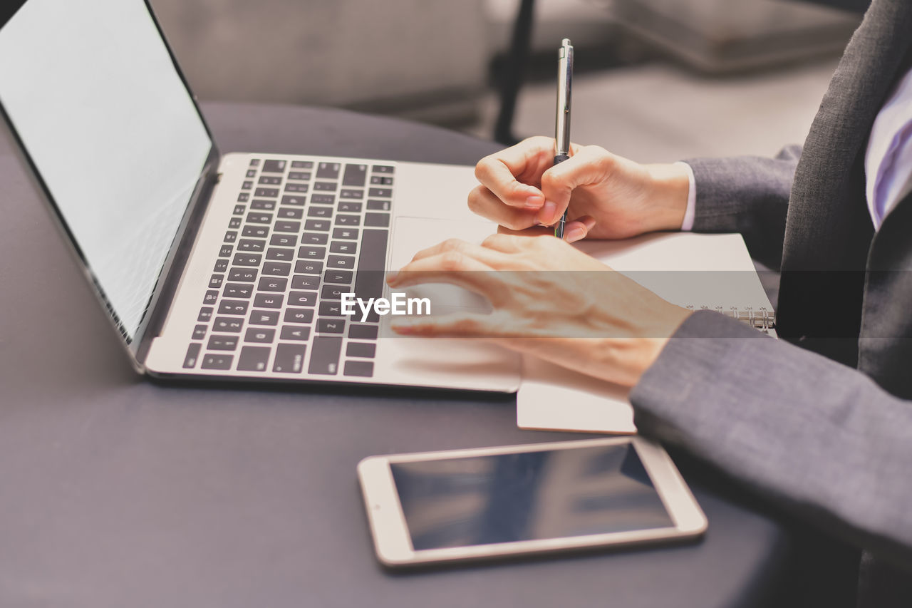 Midsection of businesswoman using laptop while writing in book