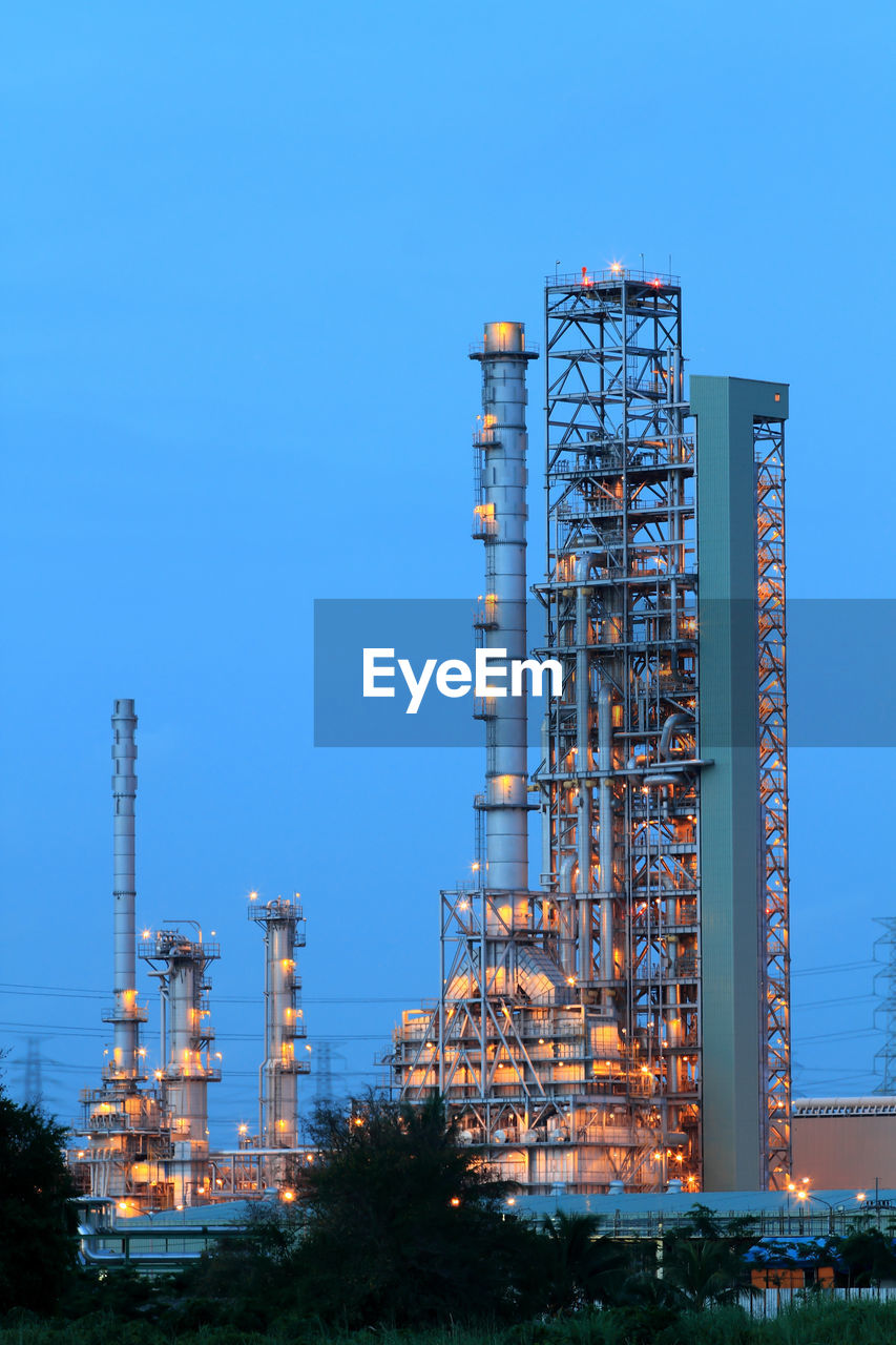 LOW ANGLE VIEW OF ILLUMINATED INDUSTRY AGAINST CLEAR BLUE SKY