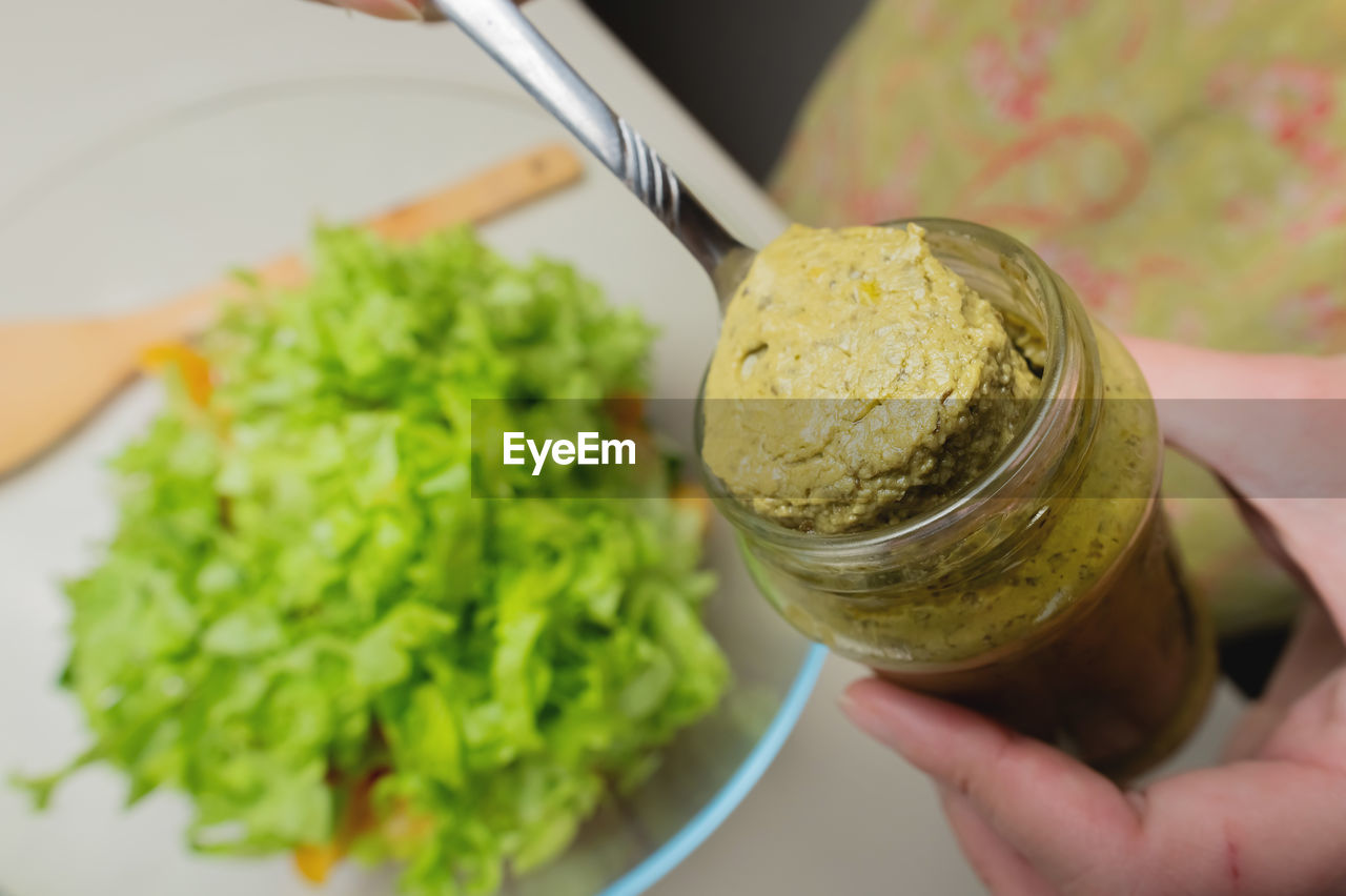 Woman's hand with a jar in the kitchen, from which salad sauce is taken out with a spoon