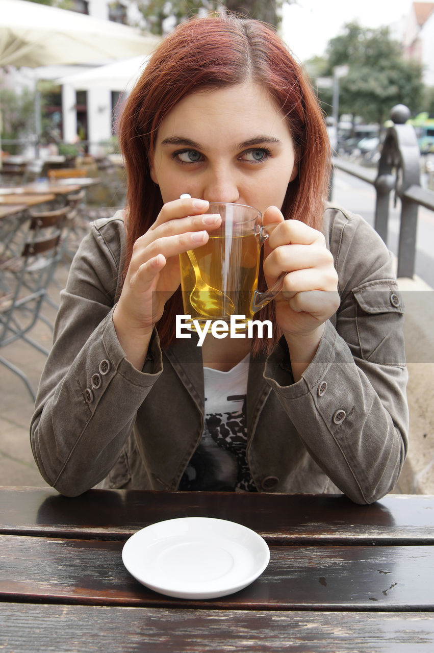 Young woman having drink while sitting at outdoor cafe