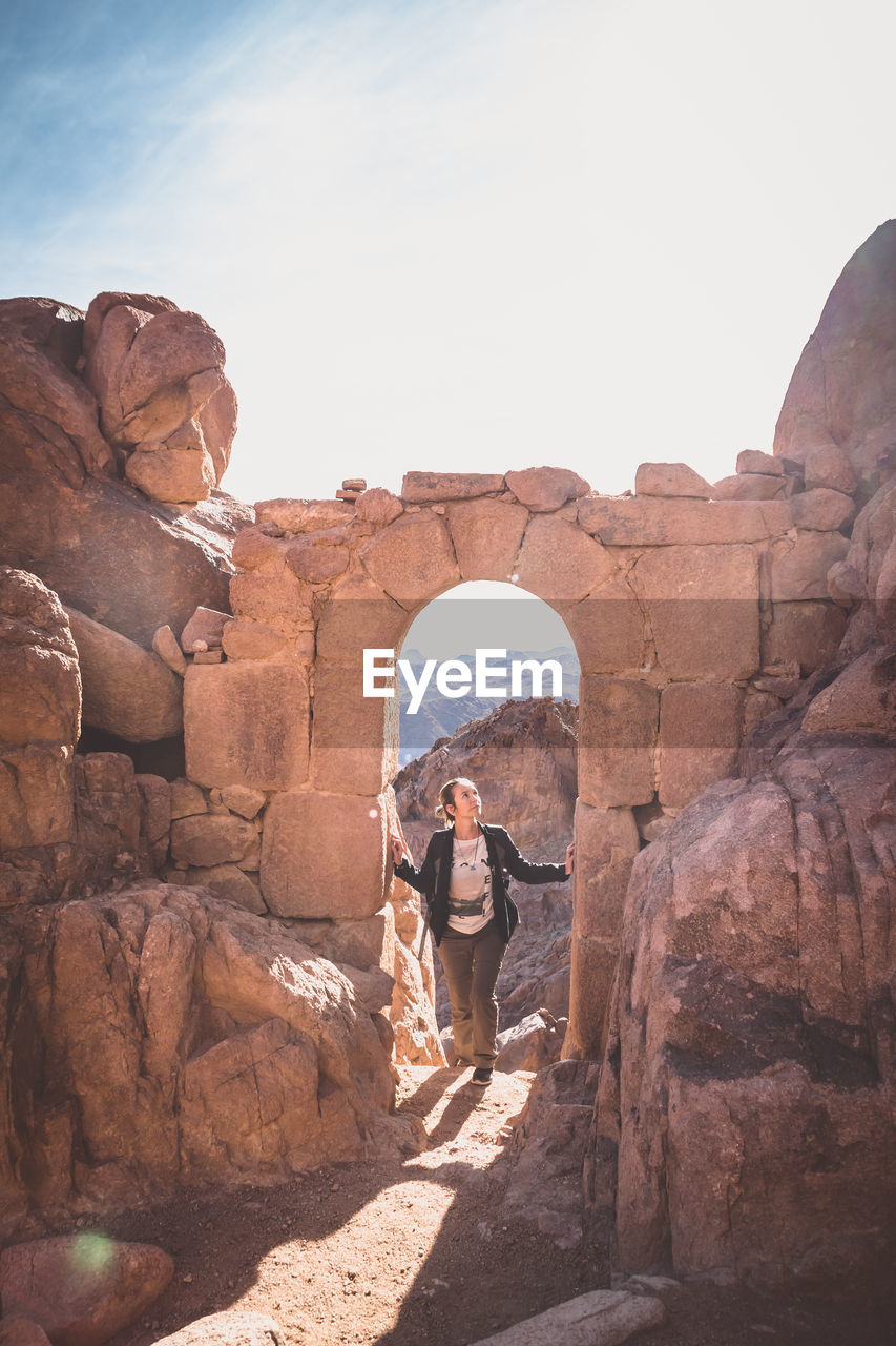 Woman standing on rock formation against sky