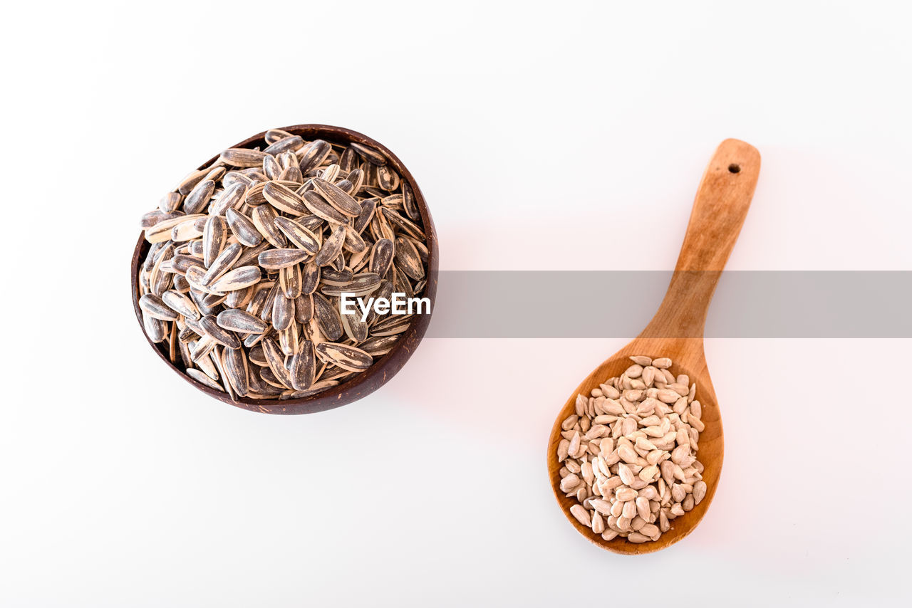 Peeled and raw unpeeled sunflower seeds in wooden spoon isolated on white background.