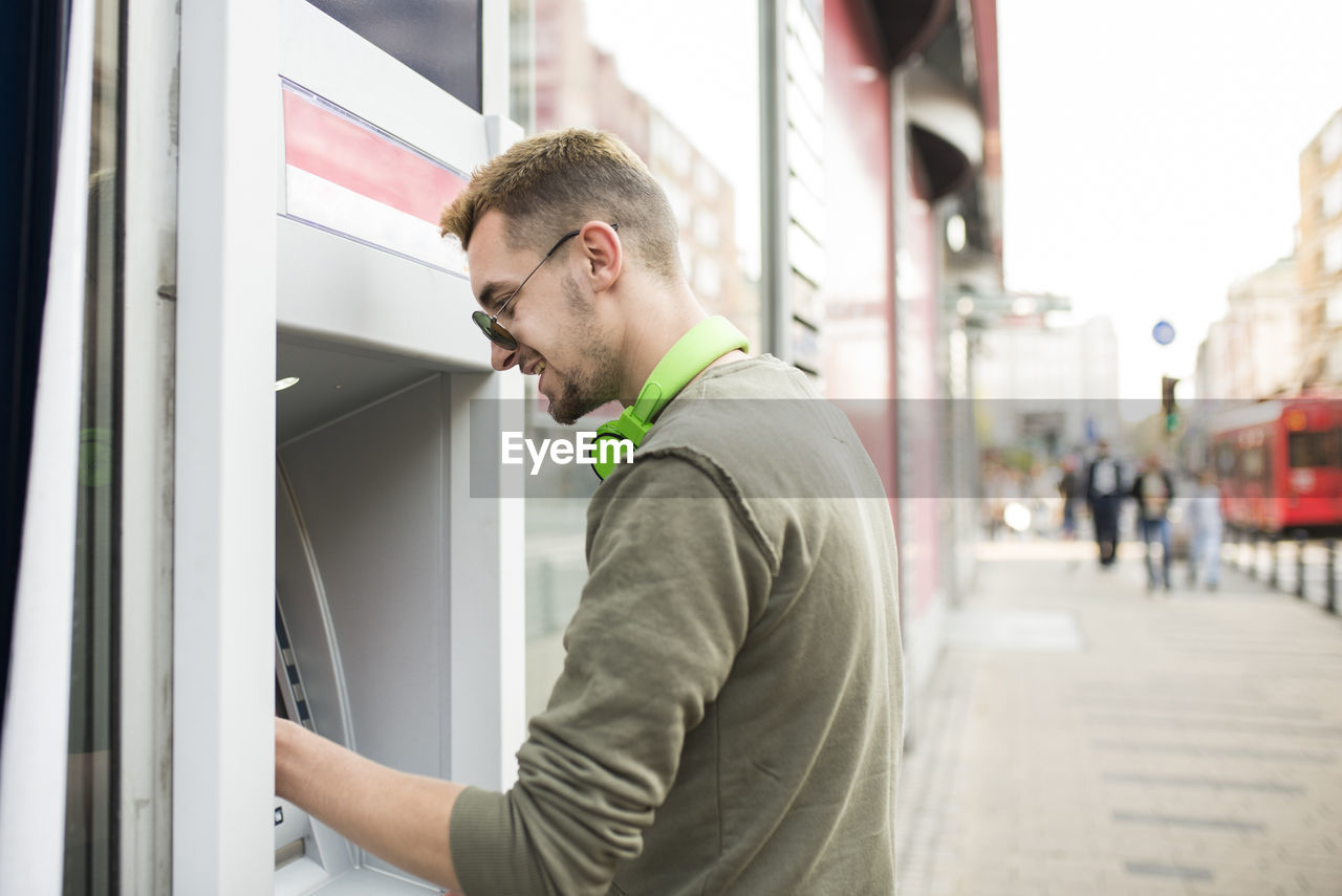 Side view of young man using atm in city