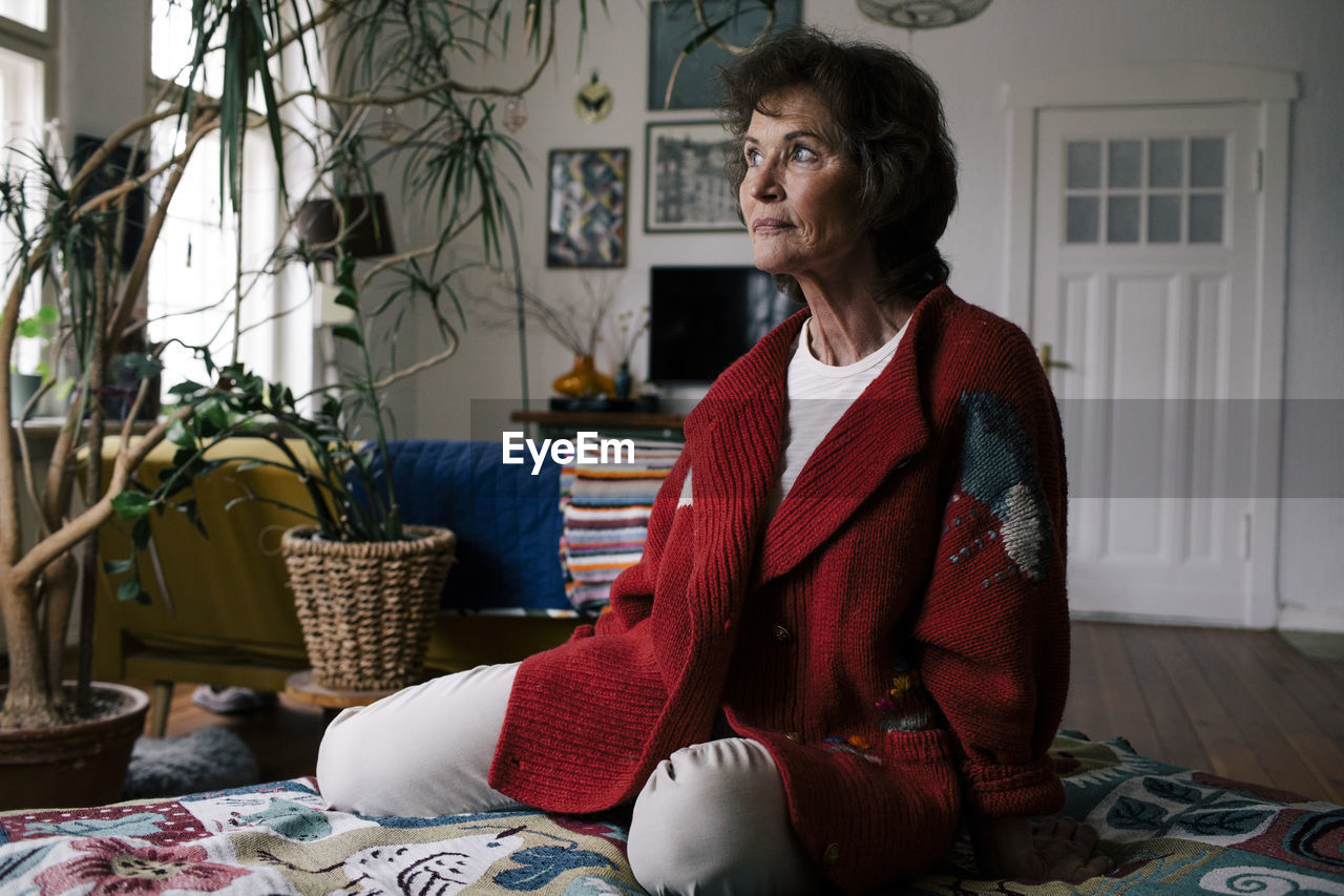 Thoughtful senior woman in sweater sitting on bed at home