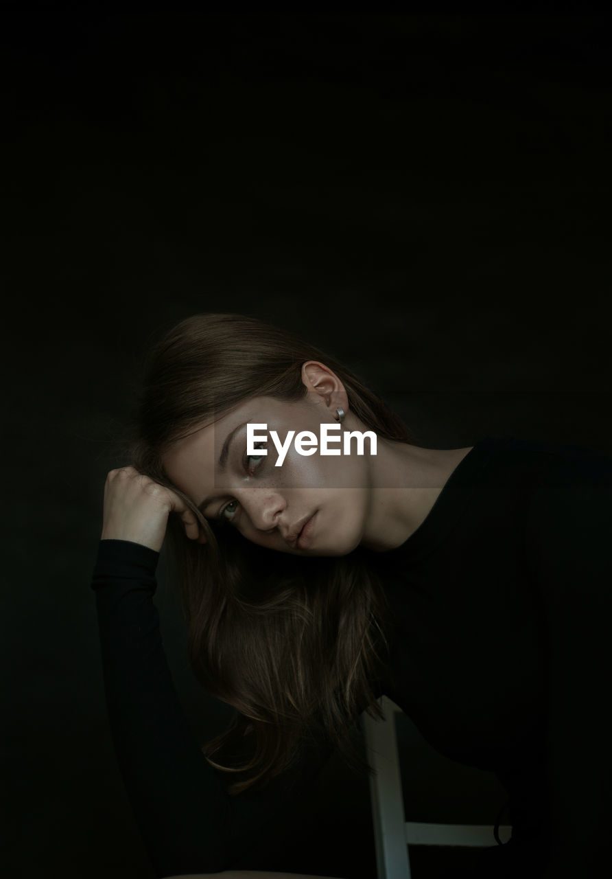 Portrait of beautiful young woman sitting against black background