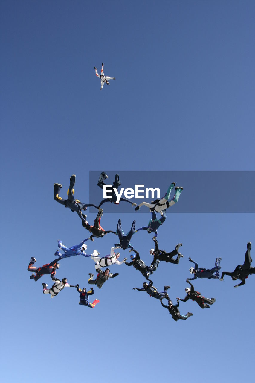 Low angle view of skydivers against clear blue sky