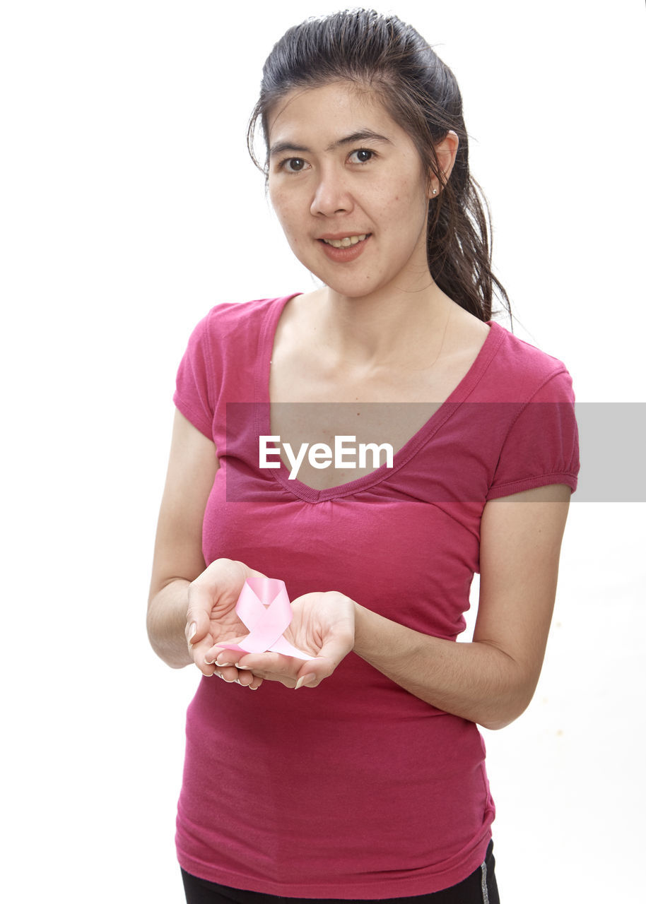 Portrait of woman holding aids awareness ribbon while standing against white background