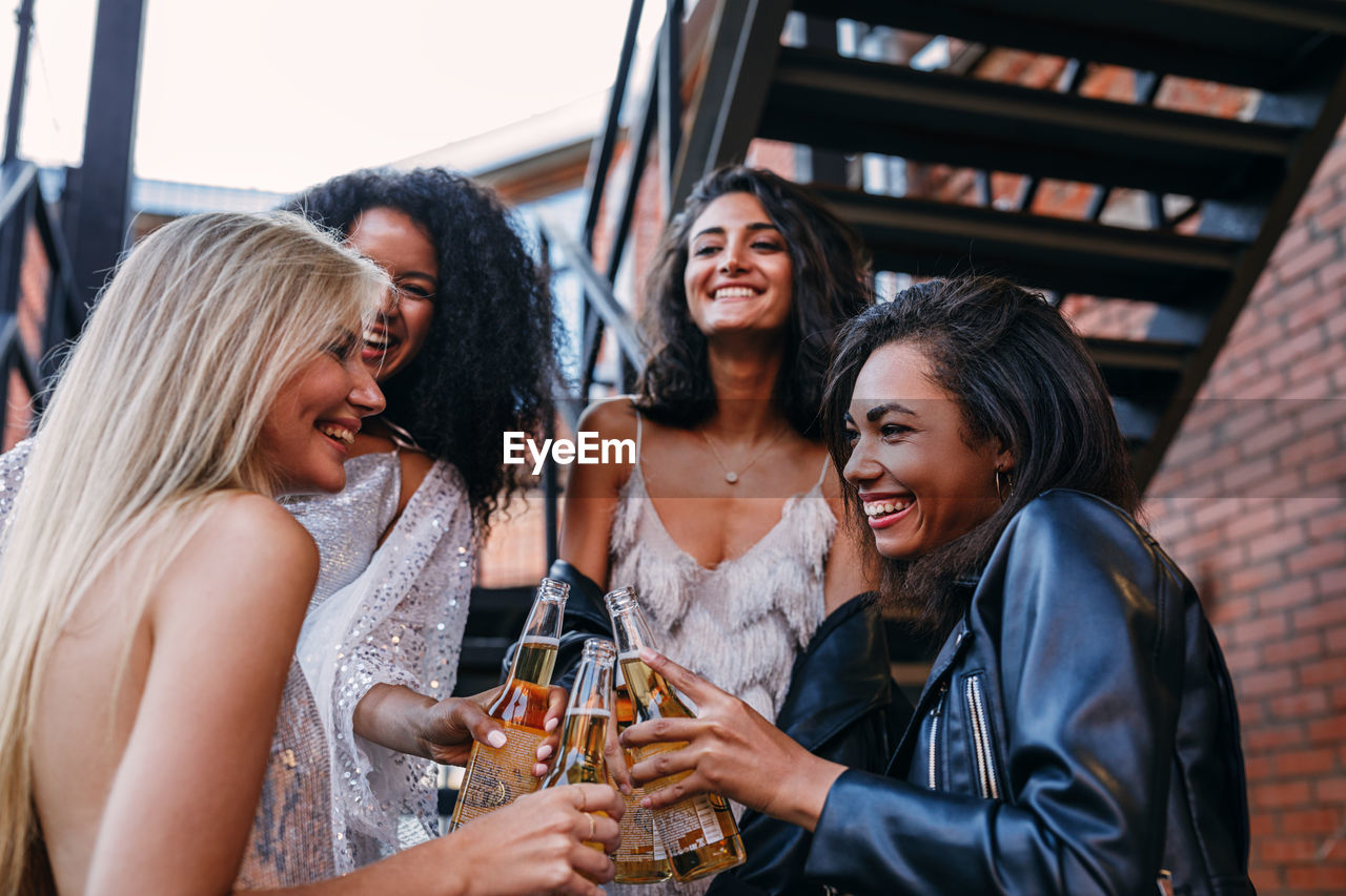 Happy friends holding beer bottle while standing on staircase